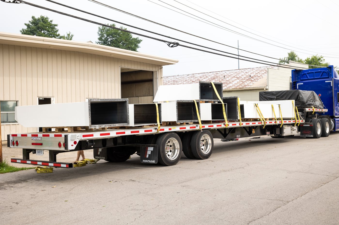 Flatbed trailer loaded with painted steel hoppers ready for delivery
