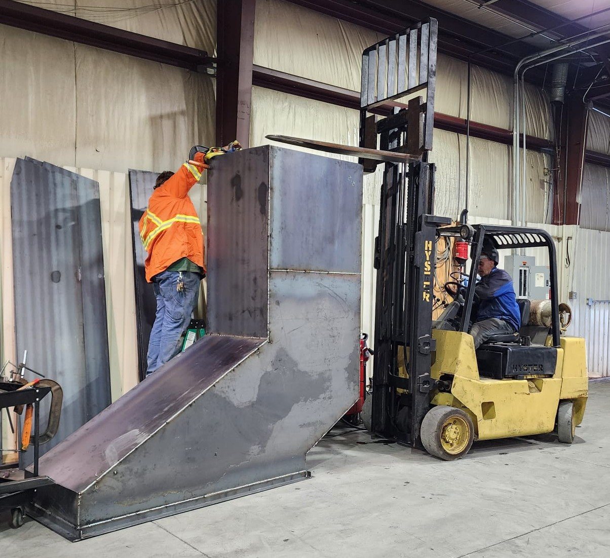 Forklift loading a steel hopper in the shop