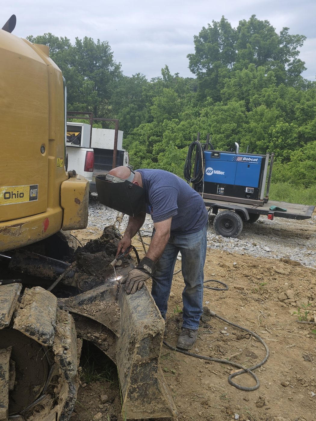 Welder repairing bulldozer track components on site